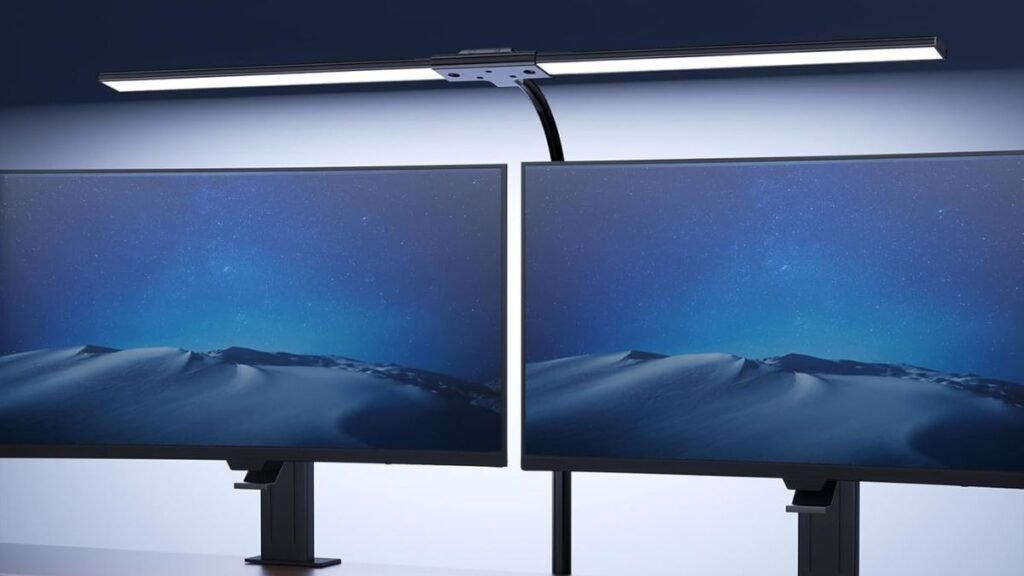 Lámpara LED instalada sobre dos monitores, proporcionando iluminación frontal uniforme en un escritorio.