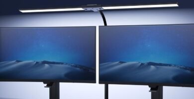 Lámpara LED instalada sobre dos monitores, proporcionando iluminación frontal uniforme en un escritorio.