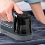 Mano usando un quitapelusas eléctrico en jersey de invierno