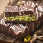 Chocolate Dubai relleno de pistacho con cobertura de chocolate y decoración blanca sobre tabla de madera