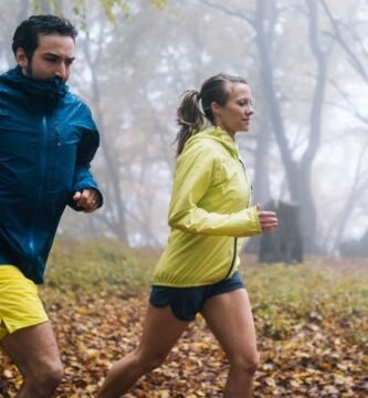 Dos corredores entrenan en un bosque con cortavientos para protegerse del frío, el viento y la lluvia